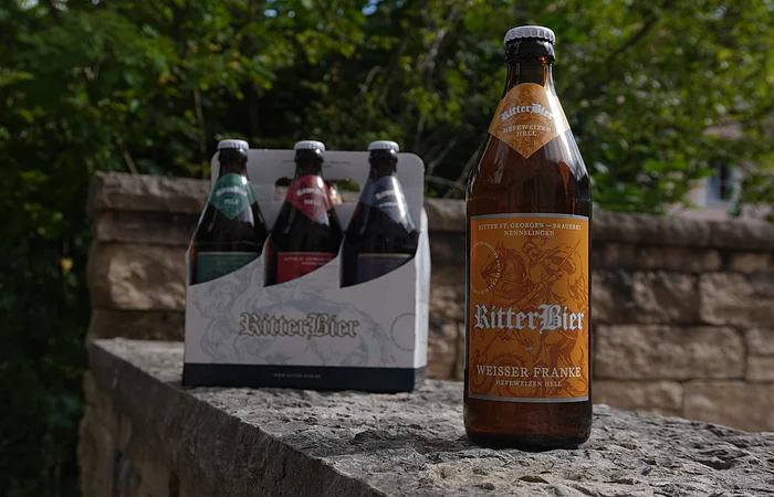 Eine Flasche Ritterbier und ein Sechserpack stehen auf einer Steinmauer im Freien.