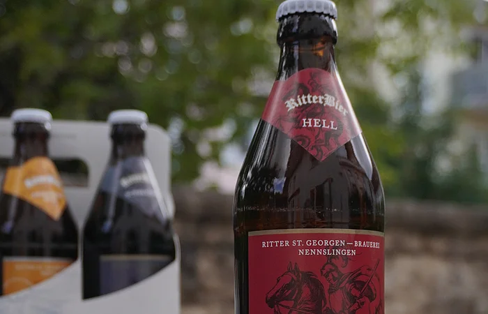 Zwei Bierflaschen mit Etiketten "RitterBier" vor einer Steinwand. Eine Flasche hat ein rotes, die andere ein blaues Etikett.