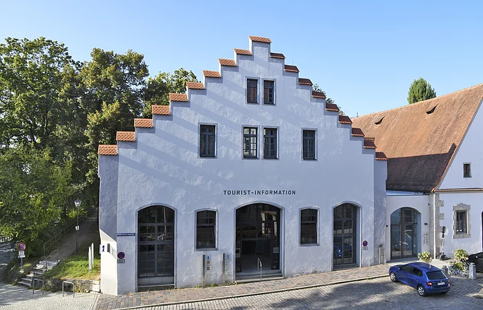 Gebäude mit Treppengiebel und Schriftzug Tourist-Information, davor gepflasterte Straße und blauer Pkw.