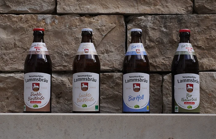 Vier Flaschen Neumarkter Lammsbräu Bier stehen vor einer Steinwand.
