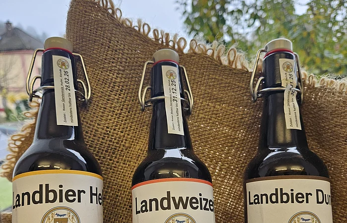 Drei Flaschen Bier mit Bügelverschluss vor Jutestoff, Sorten Landbier Hell, Landweizen und Landbier Dunkel.