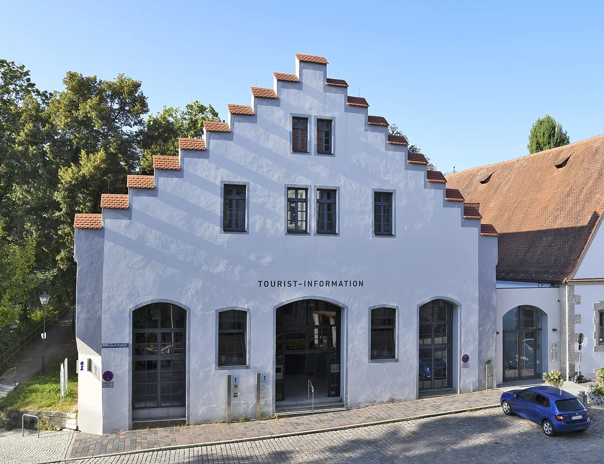 Tourist-Information Neuburg an der Donau Gebäude mit Treppengiebel und Schriftzug Tourist-Information, davor gepflasterte Straße und blauer Pkw.