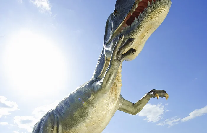 Familie mit zwei Kindern steht vor großem Dinosauriermodell im Freien bei Sonnenschein