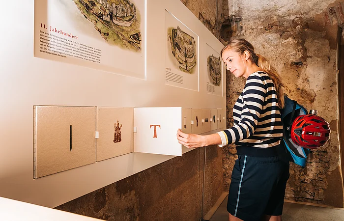 Frau in gestreiftem Pullover öffnet Klappe an Ausstellungstafel mit historischen Texten und Bildern.