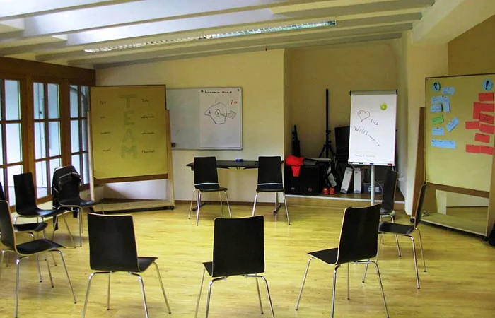 Leerer Seminarraum mit Stühlen im Kreis, Flipcharts und Whiteboards an den Wänden.