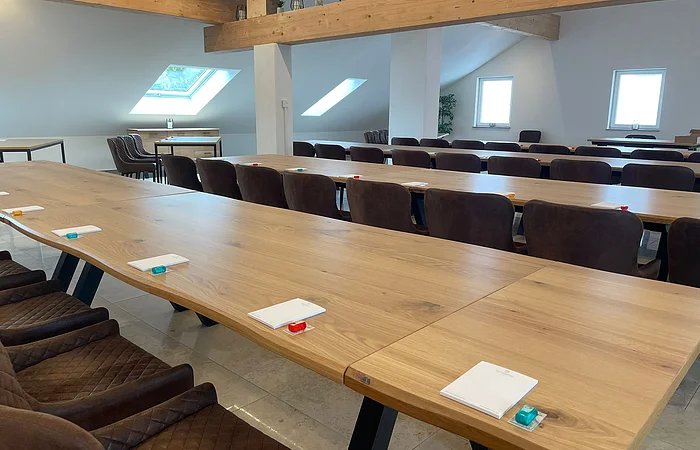 Konferenzraum mit langen Holztischen, braunen Stühlen, Notizblöcken und kleinen Gegenständen auf den Tischen.