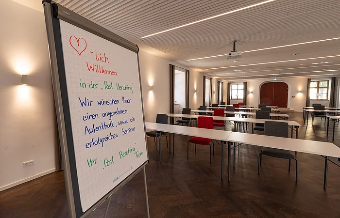 Seminarraum mit Tischen und Stühlen, Flipchart mit Willkommensgruß in der Post Berching.