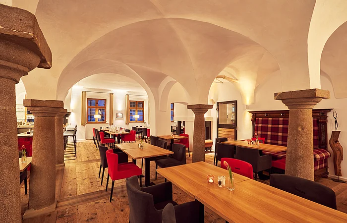 Gastraum mit Holztischen, roten und schwarzen Stühlen, steinernen Säulen und gewölbter Decke in einem Restaurant