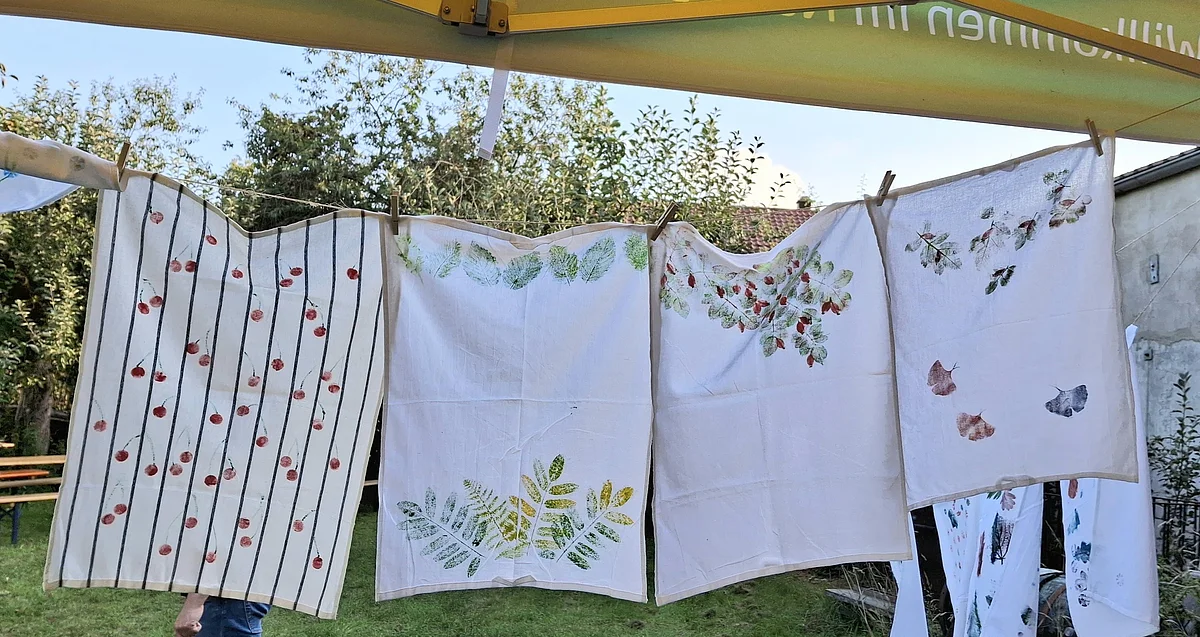 Bedruckte Geschirrtücher Vier weiße Tücher mit Pflanzenmustern hängen an einer Wäscheleine im Garten.