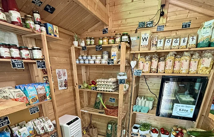 Kleiner Holzladen mit Regalen voller Lebensmittel, Eiern, Obst, Gemüse und Getränken.
