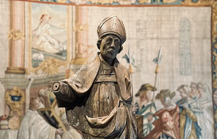 Eine Bischofsstatue steht vor einem verzierten Wandteppich