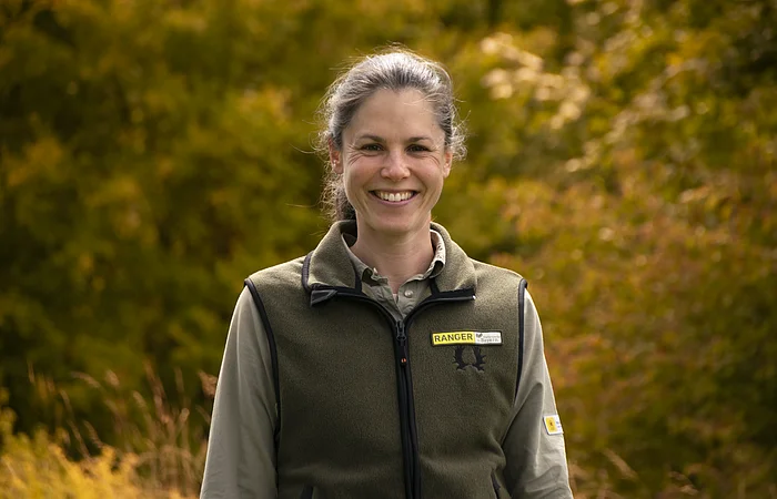 Weibliche Person vor grün-gelben Bäumen im Hintergrund