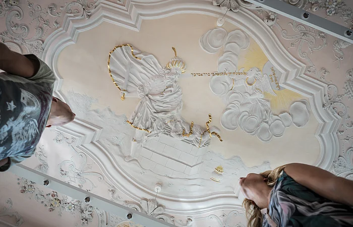 Stuckdecke im Monheimer Rathaus mit barocker farbiger Stuckreliefdarstellung und zwei Personen, die von unten darauf schauen.