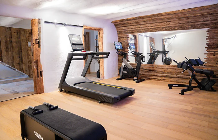 Fitnessraum mit Laufband, Fahrrad-Ergometer, Trainingsbank und großem Spiegel an der Wand.
