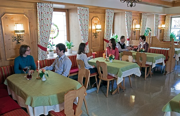 Gastraum mit Holzwänden, grünen Tischdecken, mehreren Gästen an Tischen und Kerzenlicht in einem Restaurant.