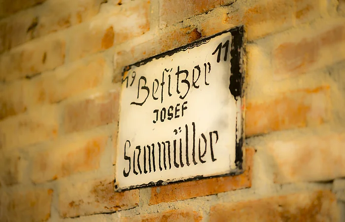 Altes Hausnummernschild mit der Aufschrift „Besitzer Josef Sammüller“ an einer Backsteinwand