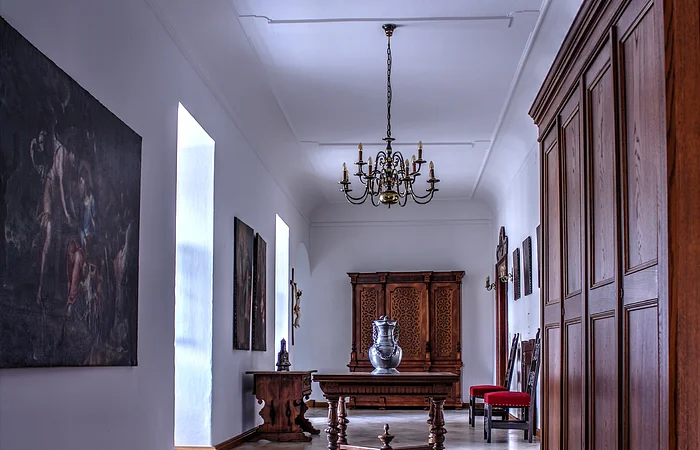 Flur mit weißen Wänden, Kachelfußboden, Holzschränken, Tisch mit Vase und Kronleuchter an der Decke.