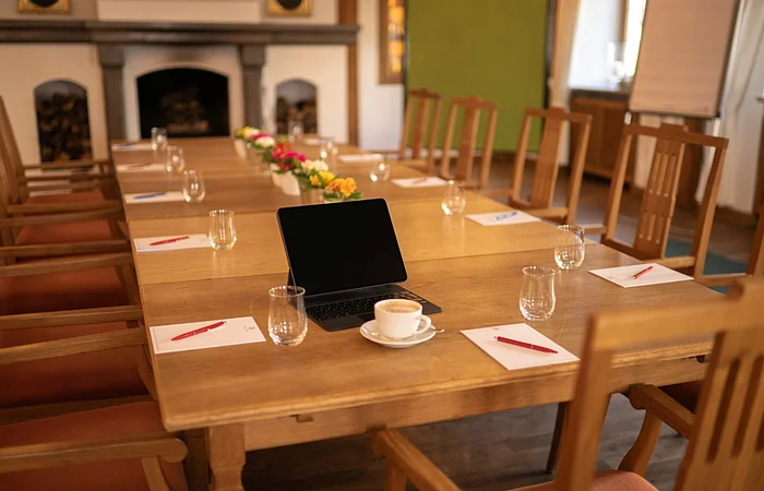 Konferenztisch mit Stühlen, Tablet, Kaffeetasse, Gläsern, Notizblöcken und Stiften in einem Raum mit Kamin.