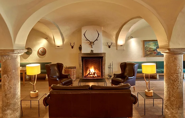 Wohnzimmer mit gewölbter Decke, Kamin, Ledersesseln, Sofa, zwei Lampen und Hirschgeweihen an der Wand.