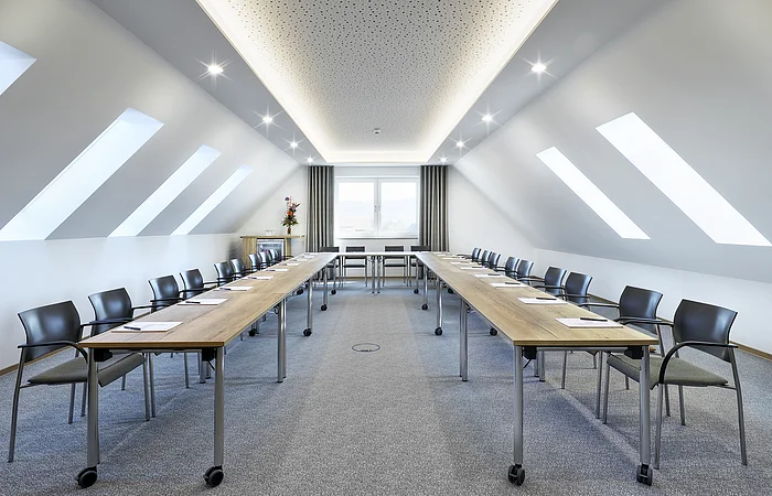 Konferenzraum mit zwei langen Tischen, Stühlen und Dachfenstern in einem hellen Raum mit Teppichboden.