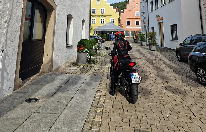 Motorradfahrer auf gepflasterter Straße mit bunten Lampions über Kopf und historischen Häusern.
