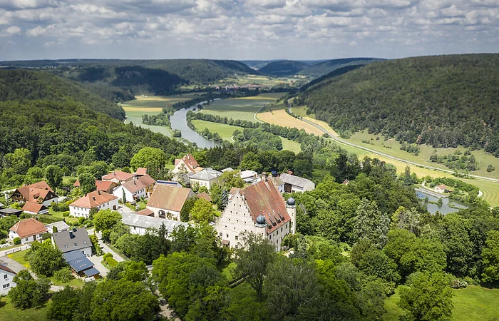 Im Vordergrund ist das Örtchen Obereggersberg mit seiner mächtigen Schlossanlage zu sehen - umgeben von Wald. Im Hintergrund öffnet sich der Blick ins Altmühltal und auf den Main-Donau-Kanal