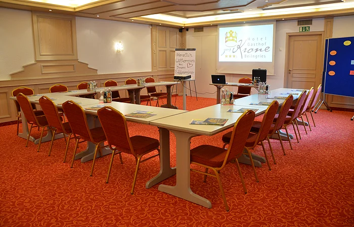 Konferenzraum mit U-förmiger Tischanordnung, Stühlen, Flipchart und Projektor mit Hotel-Logo-Beamerbild.