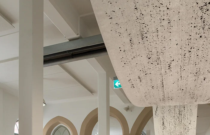 Roter weiblicher Akt-Skulptur auf weißem Sockel in hellem Ausstellungsraum mit Steinboden und Bogenfenstern.