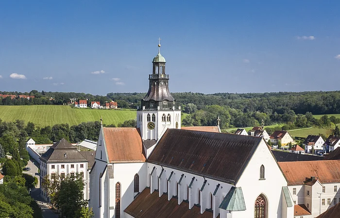 Luftaufnahme einer großen weißen Kirche mit rotem Dach in einer ländlichen Stadt bei klarem Himmel.