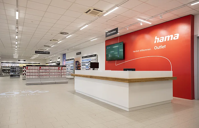 Innenansicht eines Hama Outlet Geschäfts mit Informationsschalter und Regalen für Smartphone- und Tablet-Zubehör.