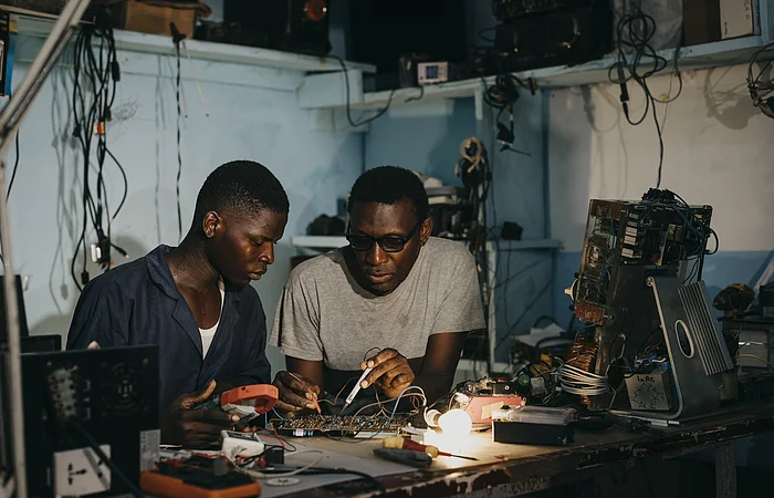 Ausbilder Bertrand Njomko repariert gemeinsam mit Azubi Silas Teyim (19)  ein technisches Geraet.