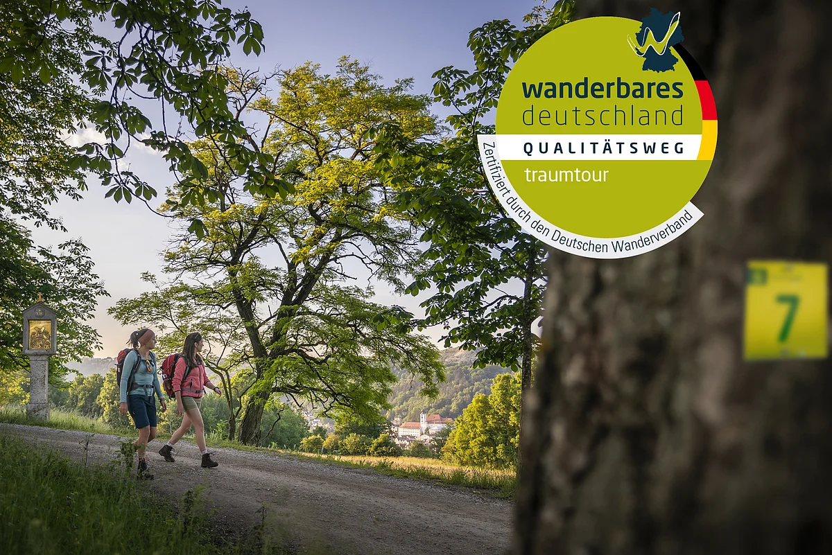 Zwei Wanderinnen auf einem Weg unter Bäumen, Wanderweg-Markierung an Stamm im Vordergrund