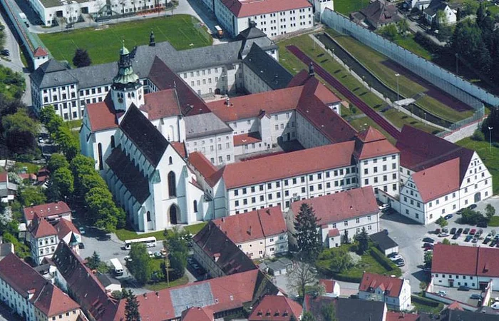 Luftaufnahme eines historischen Gebäudekomplexes mit Kirche, umgeben von Wohnhäusern und Straßen.