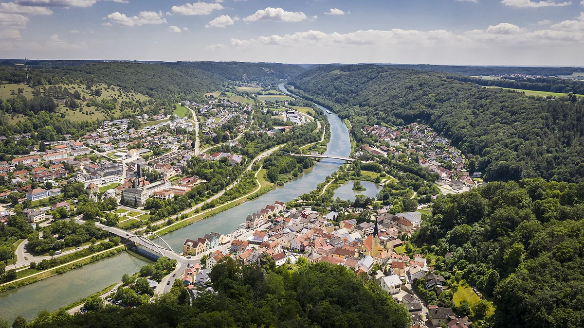 Riedenburg Der Blick auf Riedenburg von oben. Mitten durch die Stadt verläuft der Main-Donau-Kanal. Umrandet wird sie von grünen Wäldern. Der Himmel ist blau und einige Wolken sind zu sehen.