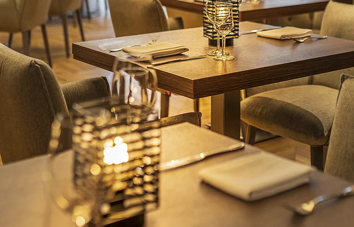 Restaurant mit gedeckten Tischen, Kerzenlicht und gepolsterten Stühlen in warmem Licht