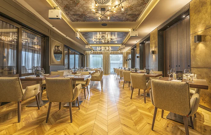 Restaurant mit Holzboden, gedeckten Tischen und gepolsterten Stühlen, Deckenleuchten und großen Fenstern
