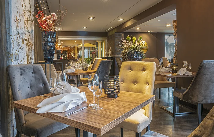 Restaurant mit Holztischen, grauen und gelben gepolsterten Stühlen, dekorativen Vasen und eingedeckten Gläsern und Servietten