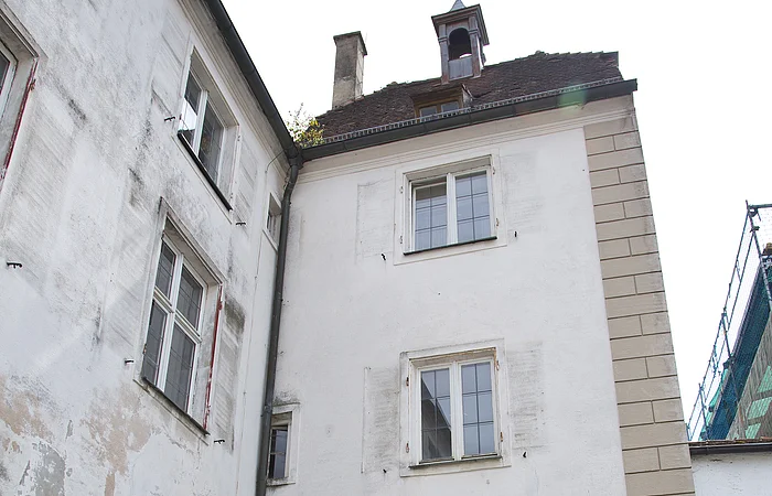Historisches Stadttor mit Durchfahrt entlang einer Kopfsteinpflasterstraße. Das Tor und das Gebäude links daneben mit einer weiß verputzten Fassade und Verkehrsschildern rechts am Torbogen. Vor dem Tor ein kleines bepflanztes Beet.