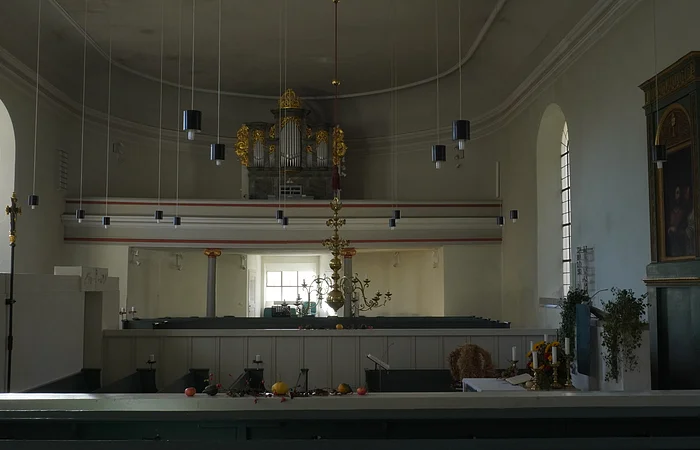 Innenraum einer Kirche mit Orgel, Kronleuchter, Kerzen und Fenstern an den Seitenwänden.