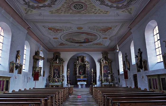 Innenraum einer Kirche mit bemaltem Gewölbedecke, Holzbankreihen und Altären mit religiösen Figuren und Gemälden