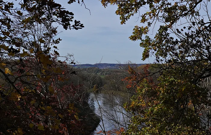 Fluss fließt durch herbstlichen Wald mit bunten Blättern unter blauem Himmel.