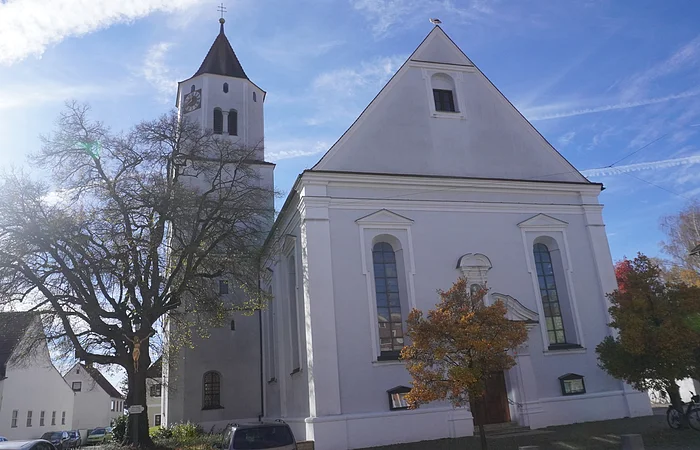 Kirche mit Turm und Bäumen im Vordergrund bei sonnigem Himmel und blauem Hintergrund.