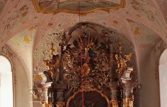 Barocker Altar mit goldverzierten Säulen, Statuen, Gemälde und verziertem Deckengemälde in einer Kirche.