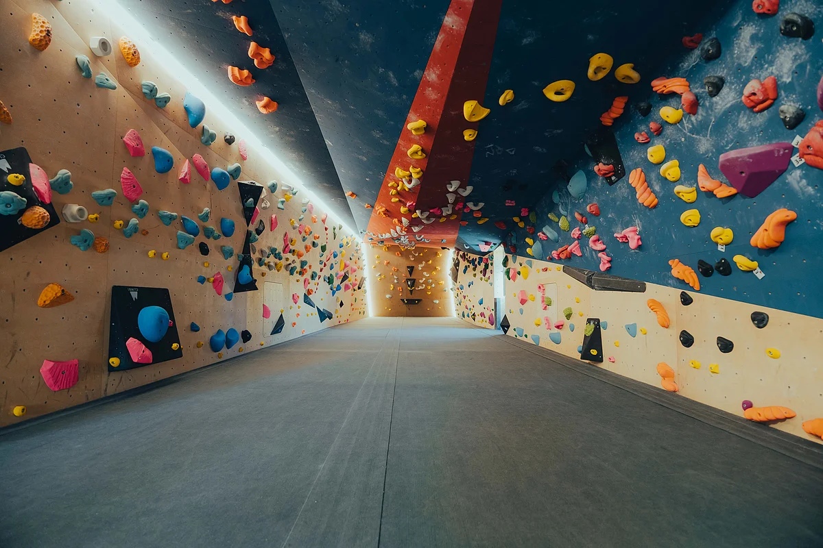 Boulderhalle Ingolstadt Leerer Kletterraum mit bunten Griffen an Wänden und Decke, gepolsterter Bodenfläche.