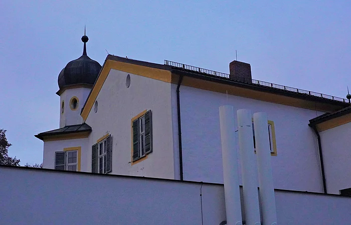 Gebäude mit weißer Fassade, grünen Fensterläden und einem Turm mit schwarzer Kuppel bei Dämmerung.