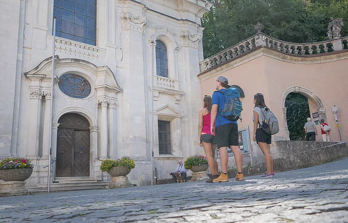 Zwei Frauen und ein Mann stehen vor der Kirche im Klosterinnenhof und bestaunen das Gebäude von außen.