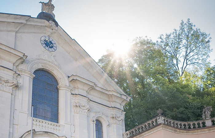 Zwei Frauen und ein Mann stehen vor der Kirche im Klosterinnenhof und bestaunen das Gebäude von außen.