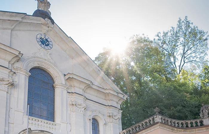 Zwei Frauen und ein Mann stehen vor der Kirche im Klosterinnenhof und bestaunen das Gebäude von außen.