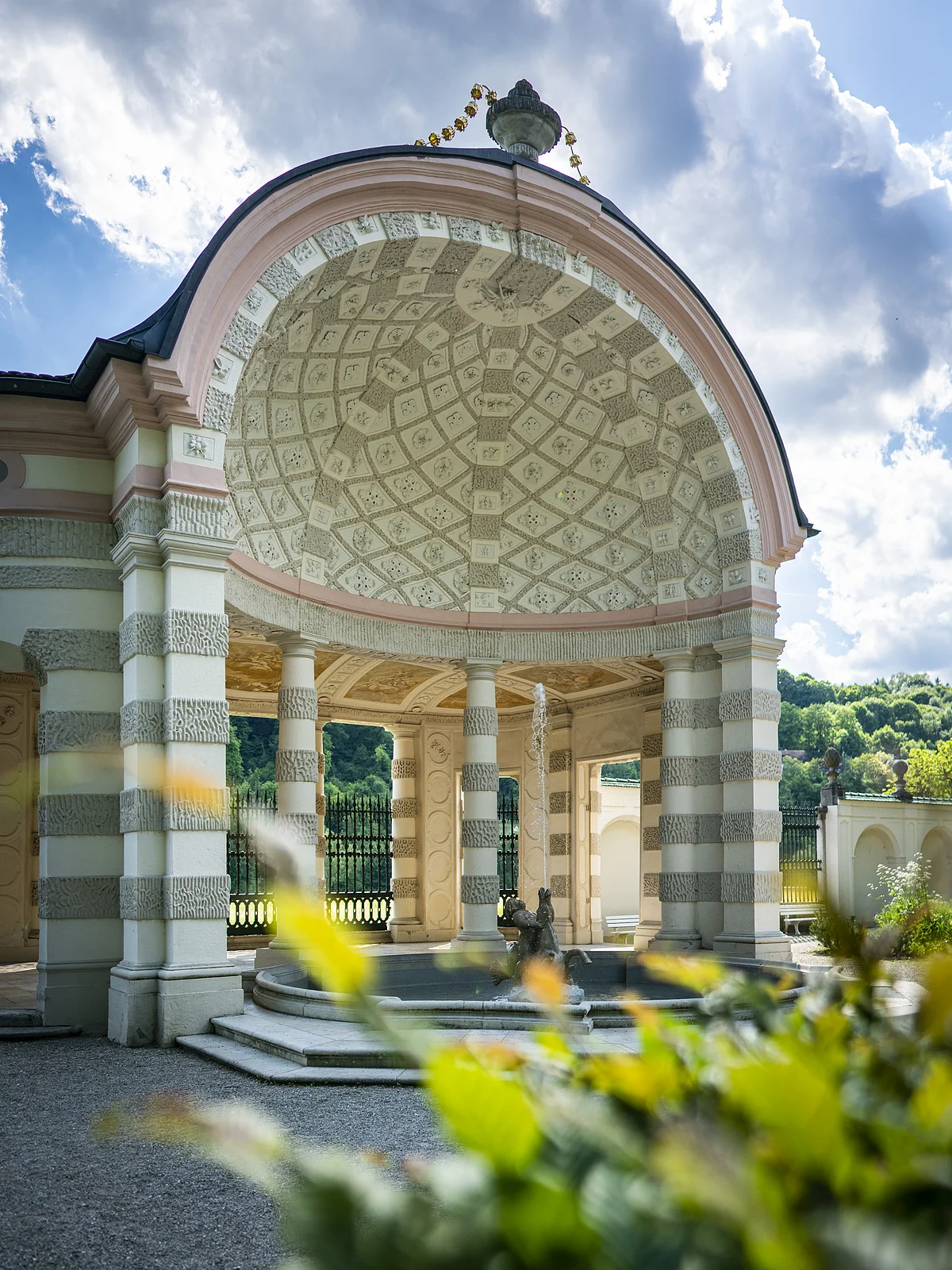Auf dem Bild ist der mittlere und größte Pavillon des Hofgartens. Der Pavillon ist rund und nach vorne hin geöffnet. Ein Brunnen befindet sich im Zentrum. Dahinter stehen mehrere weiß, grau gemusterte Säulen. Die Kuppel ist innen mit einem mosaikartigen Muster aus grauen und weißen Elementen geschmückt. Das Dach wird von einer vasenähnlichen Figur geziert.
Bildbeschreibung ehemalige Kapuzinerkirche (innen)