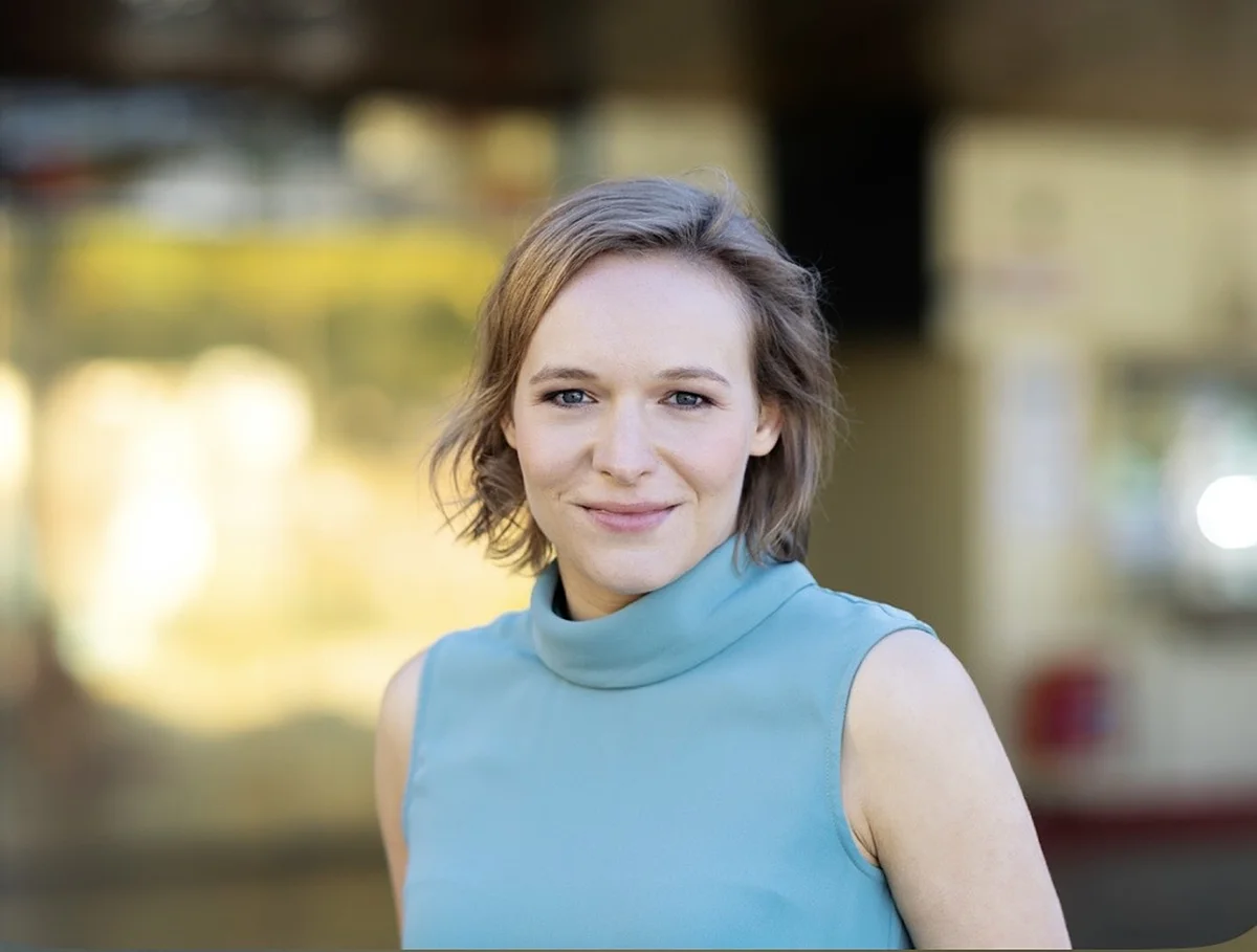 Eine Frau mit kurzen braunen Haaren und blauen Oberteil lächelt in die Kamera